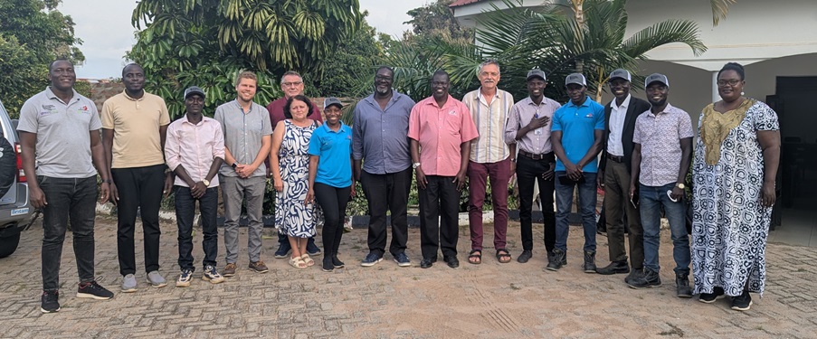 Large group standing together outdoors for a team photo in front of tropical plants and a building courtyard.